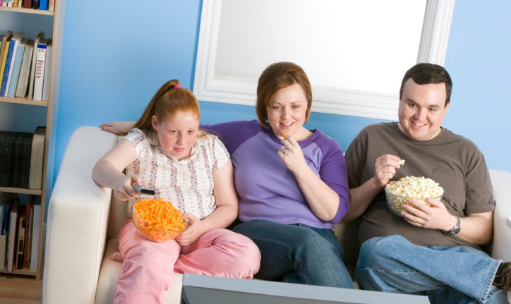 Overweight family watching television on sofa